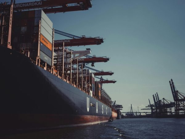A large cargo ship docked at Hamburg Harbor, cranes loading containers under a clear sky.
